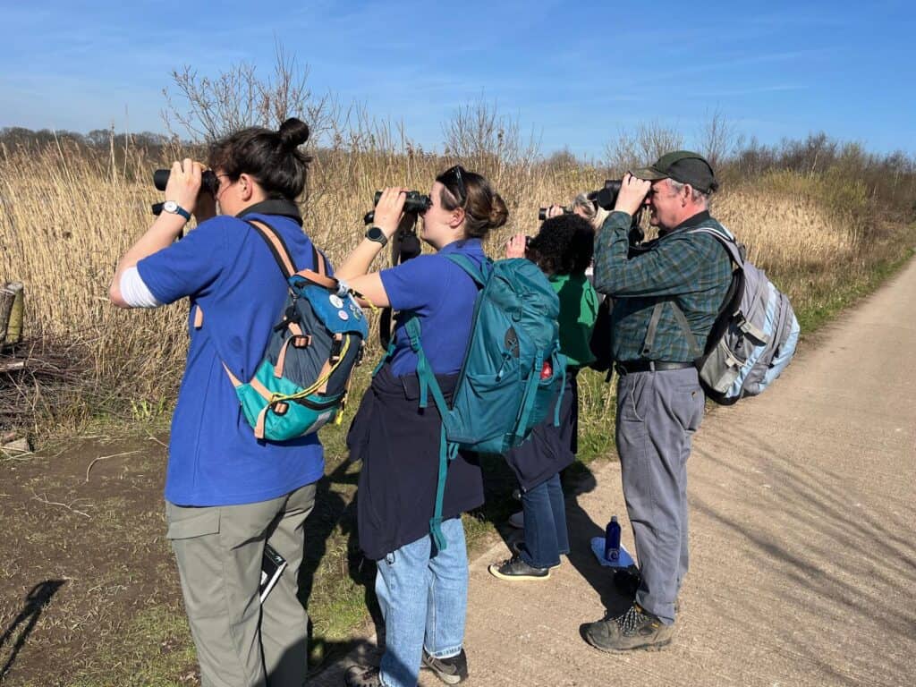 People wildlife spotting through binoculars on a river bank