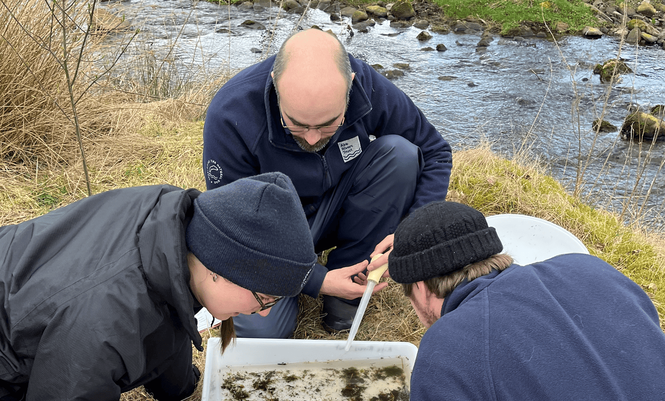 Three men looking into a tray containing a water sample