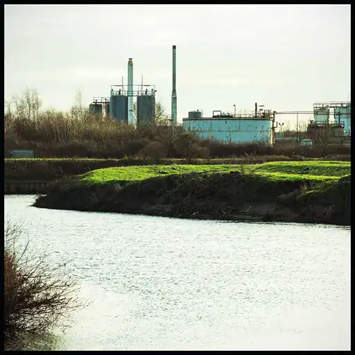 Industrial river with factory buildings and smokestacks in the background.
