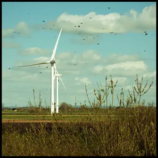 Wind turbine in a rural landscape with blue sky and clouds.