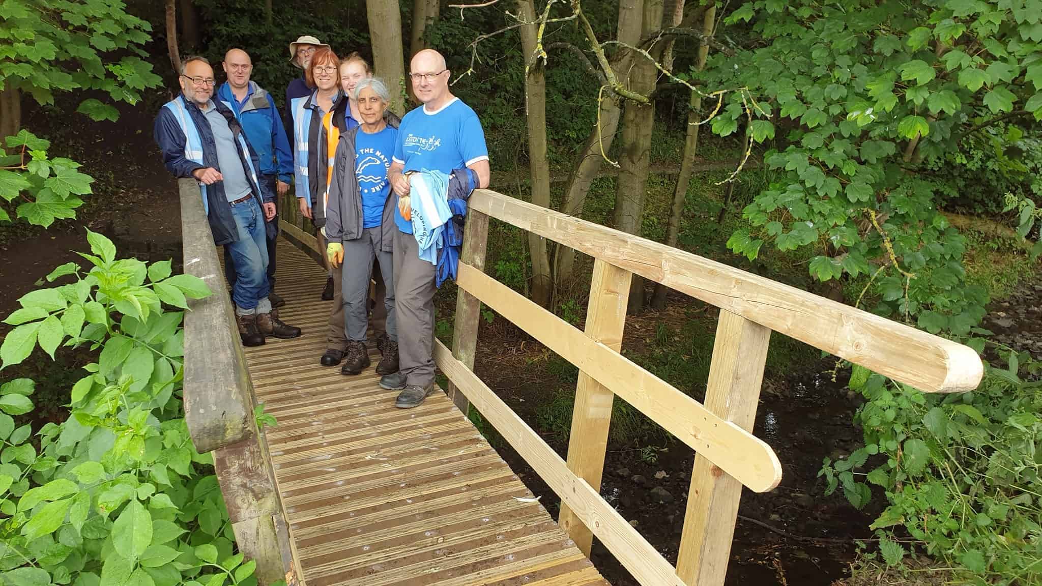 Sever volunteers standing on a bridge over a beck that they have just repaired